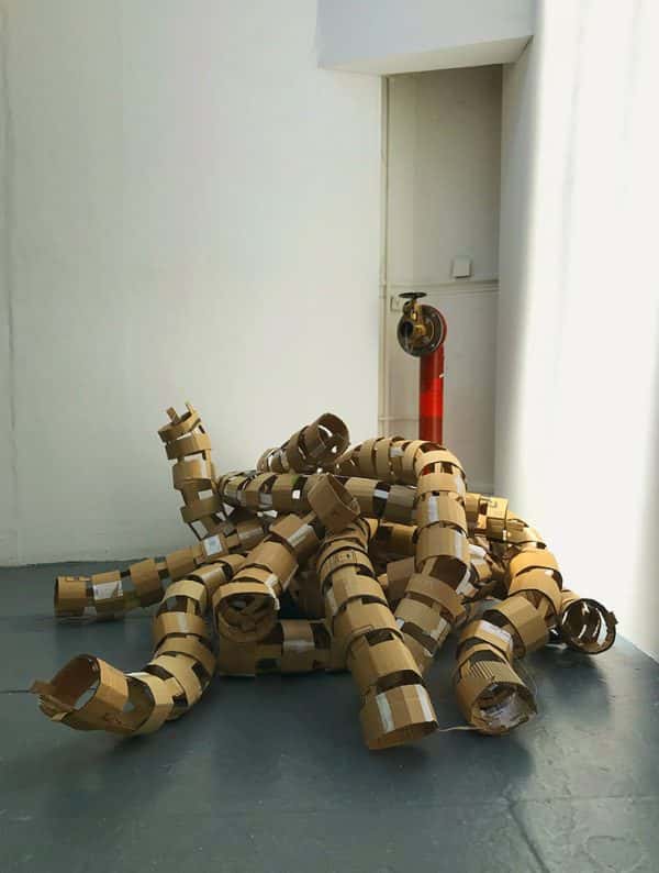 Emma Thomas - A large pile of cardboard circles grouped on the floor in front of a red water hydrant pipe.
