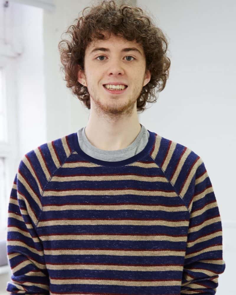 portrait photo of alum Michael Bartley smiling at camera with curly hair and blue and yellow striped jumper