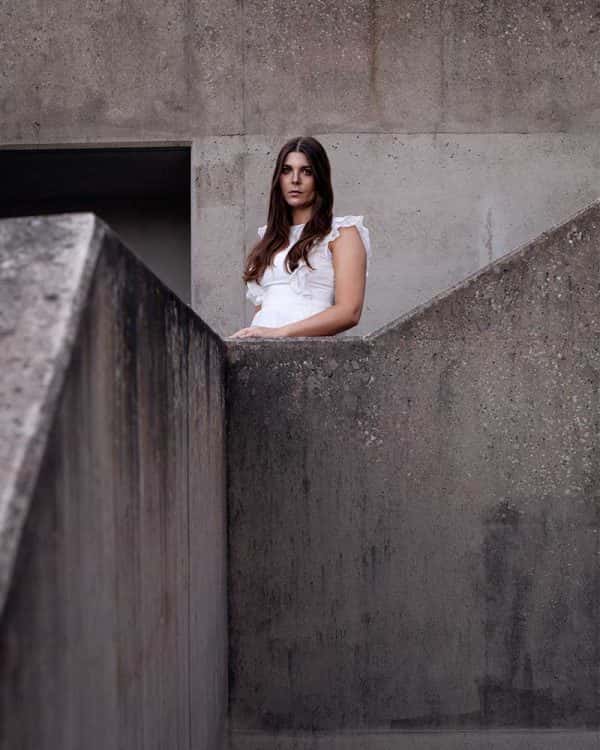 Gudbjorg Ylfa - Image of a model wearing a white dress standing amongst concrete buildings