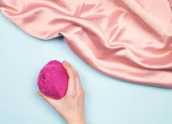 Leoni Lessman - Images of a hand holding a ball of pink thread with pink satin material