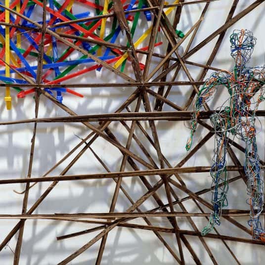  A humanoid figure made of tightly twisted wire hangs over a structure of sharp sticks