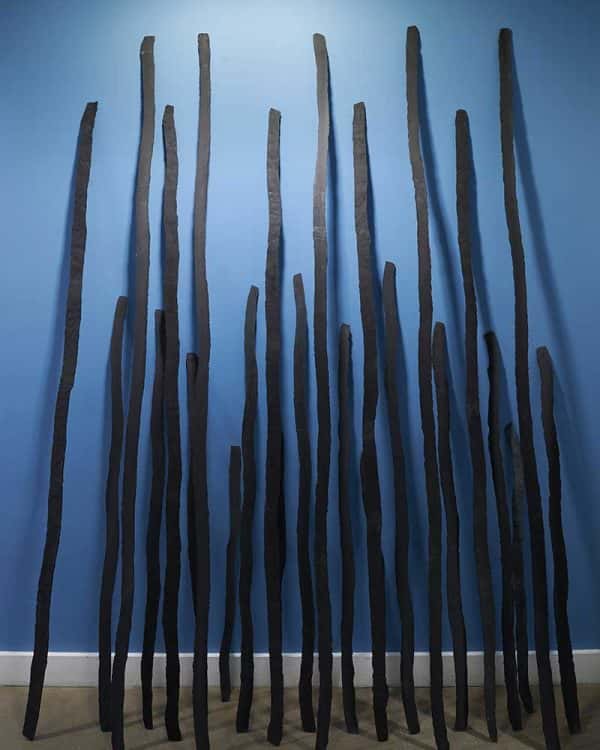 Melissa Pierce Murray - Image of several flint poles leaning against a bright blue wall, the sculpture has been created by NUA MA Fine Art student Melissa Pierce Murray