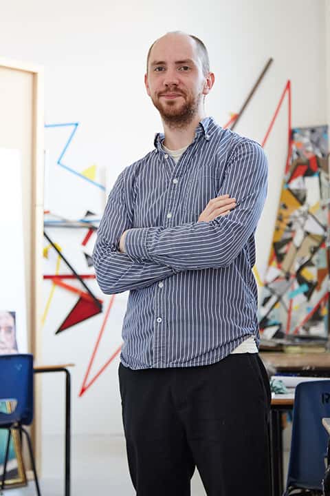 portrait photo of senior lecturer craig barber standing with arms crossed and looking at camera with short brown hair and a long sleeved vertically striped blue and white shirt