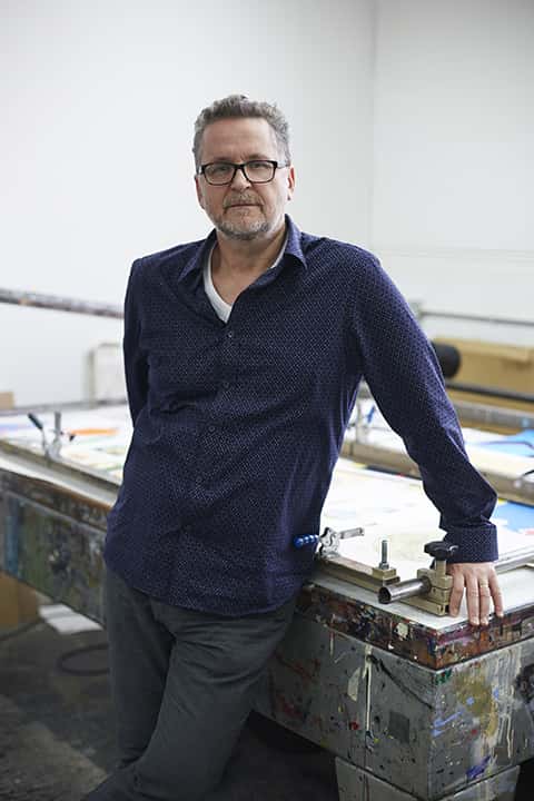 photo of course leader Carl Rowe standing with arms leant against a printing table and looking at camera with short hair and a blue shirt with a small lattice print