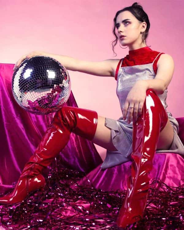 Sophie Chittock - image of a model sitting wearing red thigh high boots and holding a disco ball