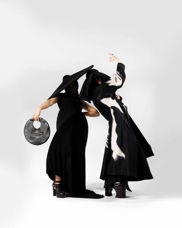 Emily Rose - Two figures strike a pose in long monochrome dresses, with their faces obscured by the shadows from their extremely wide-brimmed hats. Together, their silhouette is almost a circle on the white background