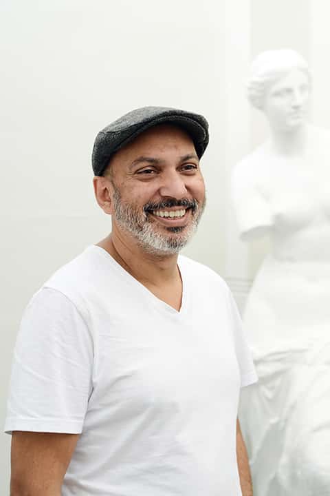 portrait photo of lecturer Suri krishnama smiling and looking away from camera with grey flat cap and a white t-shirt