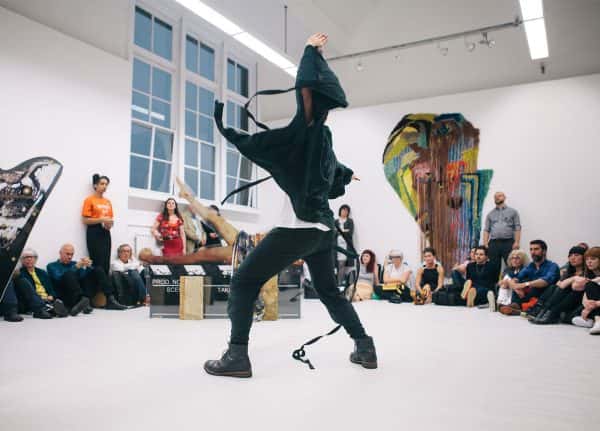 British Art Show 8 at NUA - Image of student in black and white clothing performing in front of a seated audience at the British Art Show 8 Exhibition
