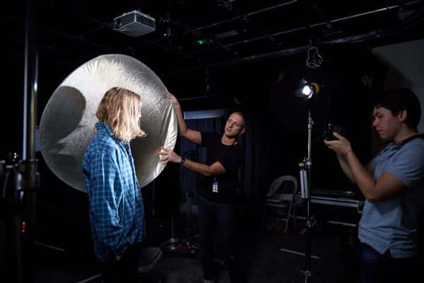  - Photography setup in a dark room, with a white diffuser being held behind a model