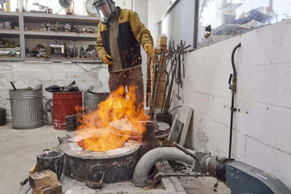  - A technician in the foundry stands over a flaming furnace