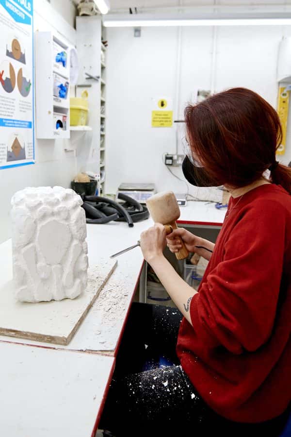  - A student in the 3D workshop chips away at a block of plaster using a mallet and chisel