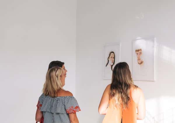  - Photograph of three people looking at painted portraits in 2017 BA Degree Show