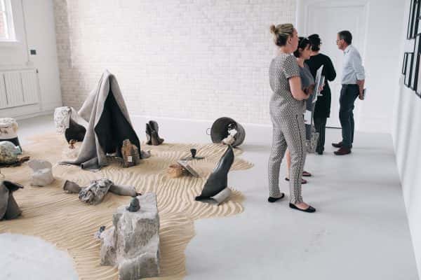  - Sculptures in the middle of the room on sand with people looking at work on the walls