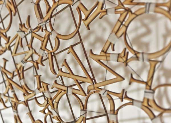 Kirsty Campbell - Image of lasercut wooden letters hanging on a wall, stitched together with tape