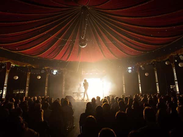Norfolk and Norwich Festival - Image of a performer on a stage in front of a back lit audience and under a red canopy