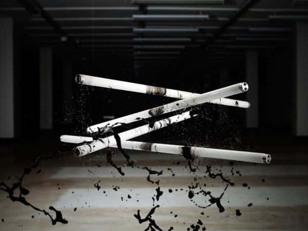 Simon Bell - Image of four tubes of strip lighting hanging in the air with black paint being dropped on them from above