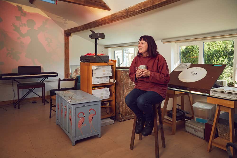 Suzie Hanna professor of Animation sitting on a stool with a cup of tea in her home-made animation studio