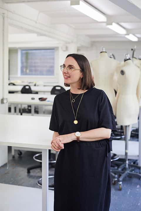 BA Fashion Lecturer Nina Dobson standing in front of two mannequins in the Norwich University of the Arts Fashion studio