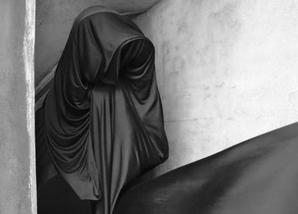 Emily Cannell, MA Fashion - Monochrome photo of a figure draped in swathes of dark fabric against a stone background
