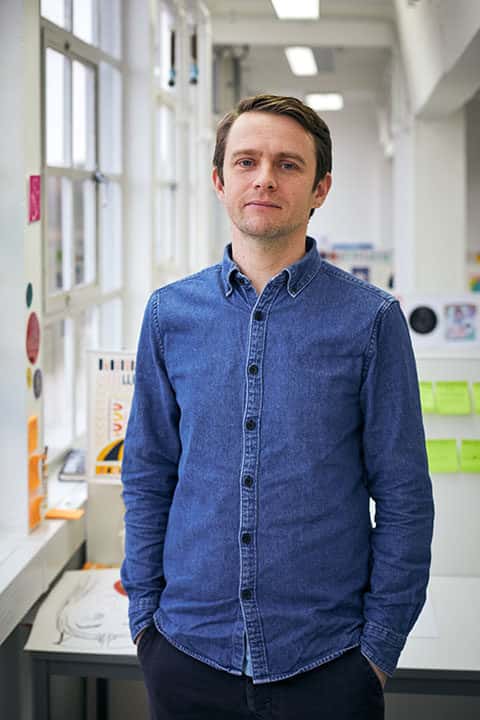 BA Illustration Lecturer Rob Nicol standing in an illustration studio at Norwich University of the Arts wearing a denim shirt