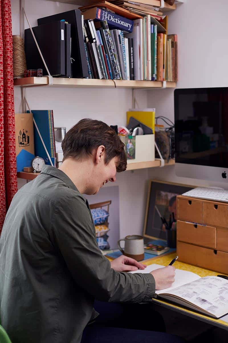 Kate Farley working in her home studio in front of shelves of books