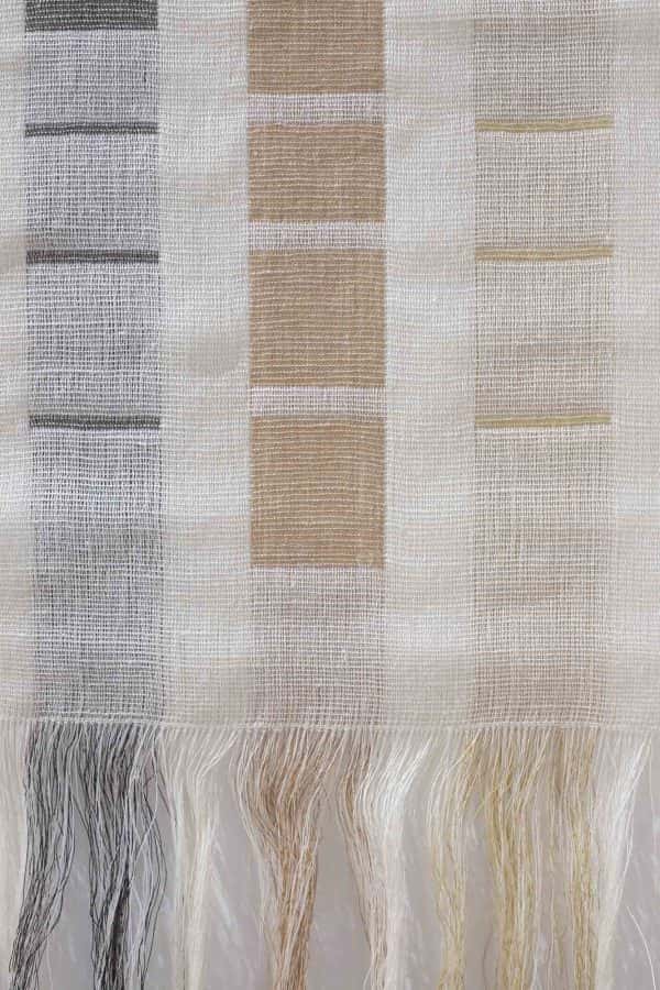 Lizzie Kimbley - Close up of a woven textiles piece hanging on a white wall and made up of grey and pale rust squares on a cream background