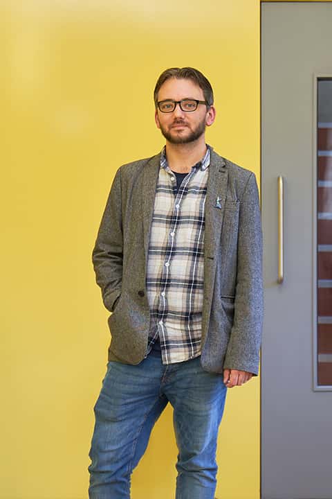 BA Animation Lecturer Dan Root standing in front of a yellow wall