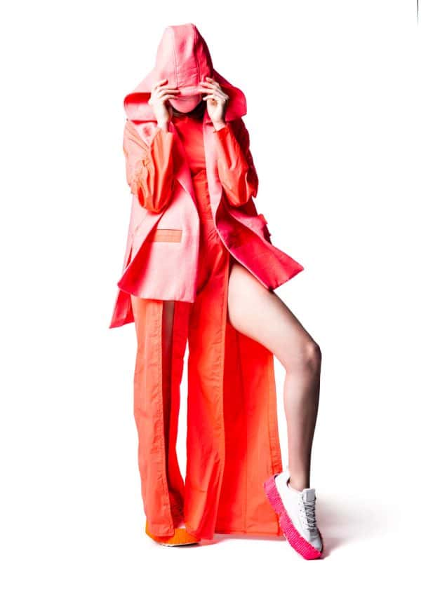 Annabelle Shortland - A female model wears a floor length neon pink split leg jumpsuit, with a neon pink jacket, hood up covering her face. Garment designed by BA Fashion student Annabelle Shortland