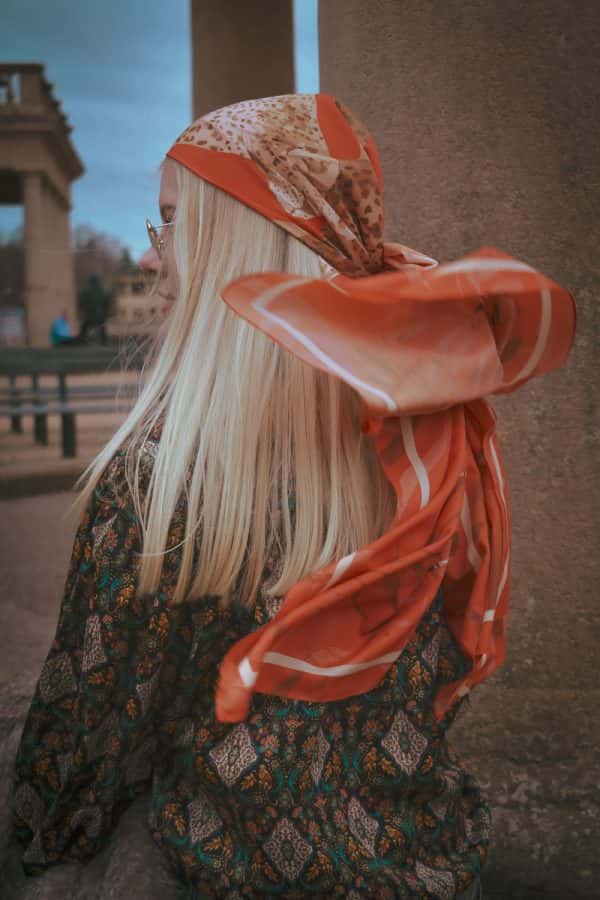 Amy Foster - A photograph from behind a female model with long blonde hair, wearing a red and white headscarf, which has caught the wind. Styled and photographed by BA Fashion Communication and Promotion student Amy Foster