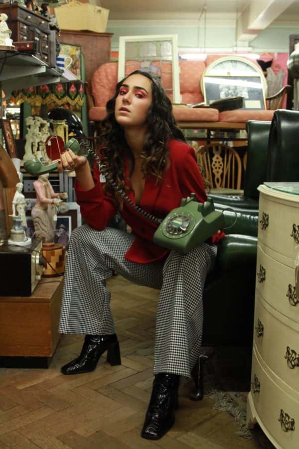 Ana Corona - Photo of a brunette female model sat in an old antiques shop, leaning forward, holding a green corded telephone in her hand. Styled and photographed by BA Fashion Communication and Promotion student Ana Corona