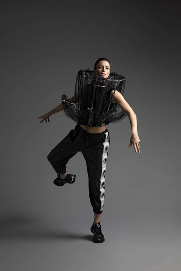 Katie Bilingsley - Model is balanced in motion like a puppet on strings, and is wearing a cylindrical metal frame supported by their neck, which extends out at chin level, and down to the belly where it branches out to create a peplum with the metal skeleton, draped with black mesh