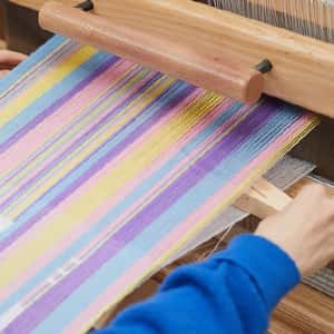 A loom with thread set up, the thread is yellow, pink, blue, and purple