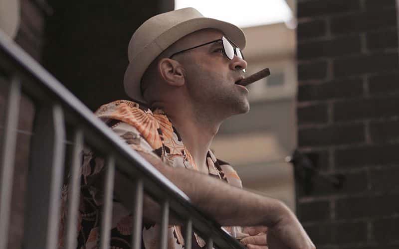 Image showing person smocking cigar on balcony wearing hat and sunglasses